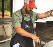 Man grilling on deck wearing the red and white recteq Patriotic Signature Line hat, the recteq premium apron and has the recteq instant read thermometer in apron pocket. 